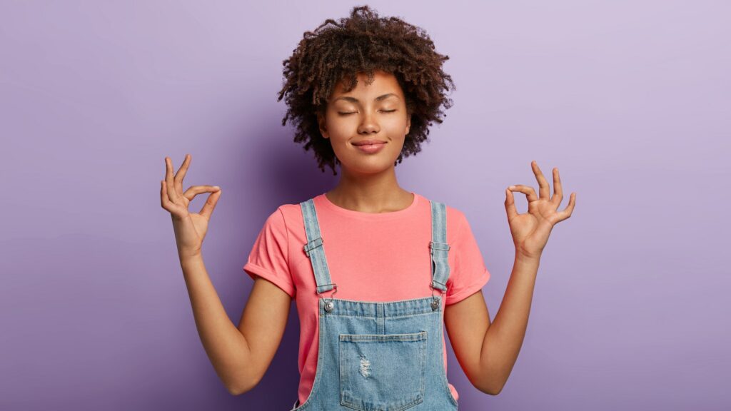 Relaxed calm woman gathers patience, meditates and makes mudra gesture, breathes deeply, holds hands